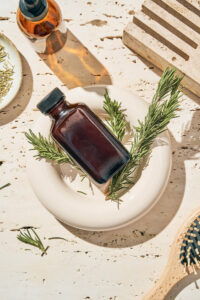 A dark brown glass bottle on a small tray with rosemary sprigs.