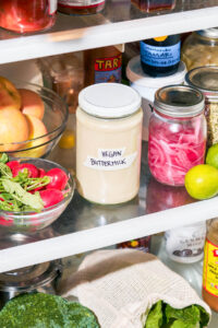 A jar labeled vegan buttermilk in a fridge with other jars and vegetables.