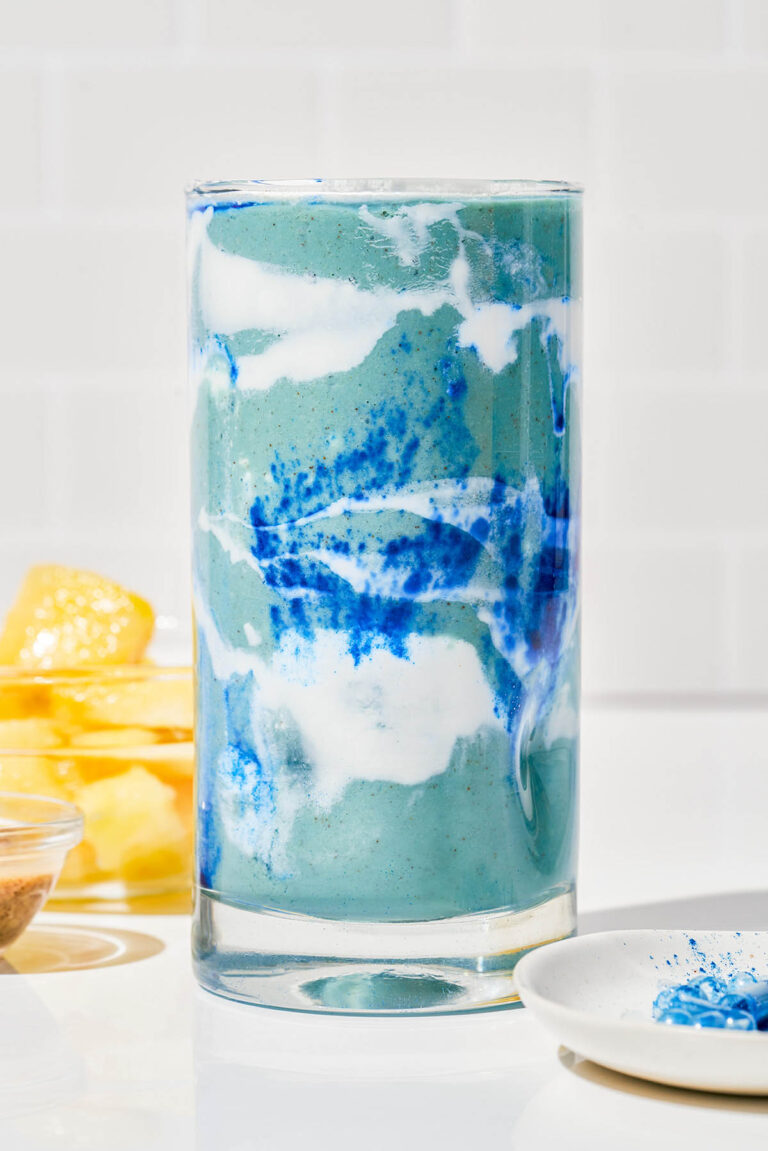 Straight-on of a glass filled with green, blue, and white smoothie to look like clouds.