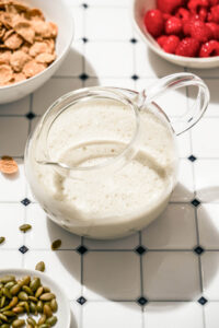 A jug of milk on a tile surface with cereal ingredients around.