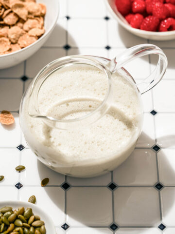 A jug of milk on a tile surface with cereal ingredients around.