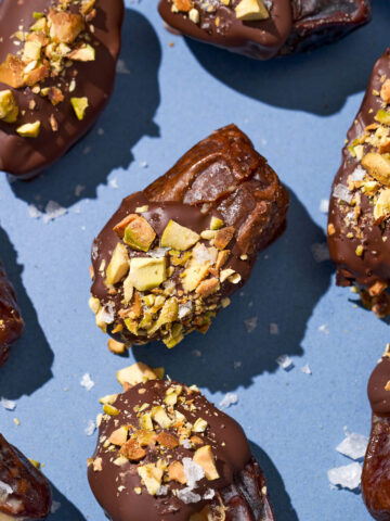 Close up of filled dates dipped in chocolate with pistachios on a blue plate.