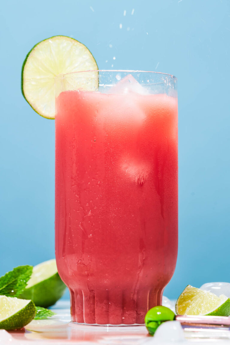 Pink smoothie on a blue background with a lime wedge.
