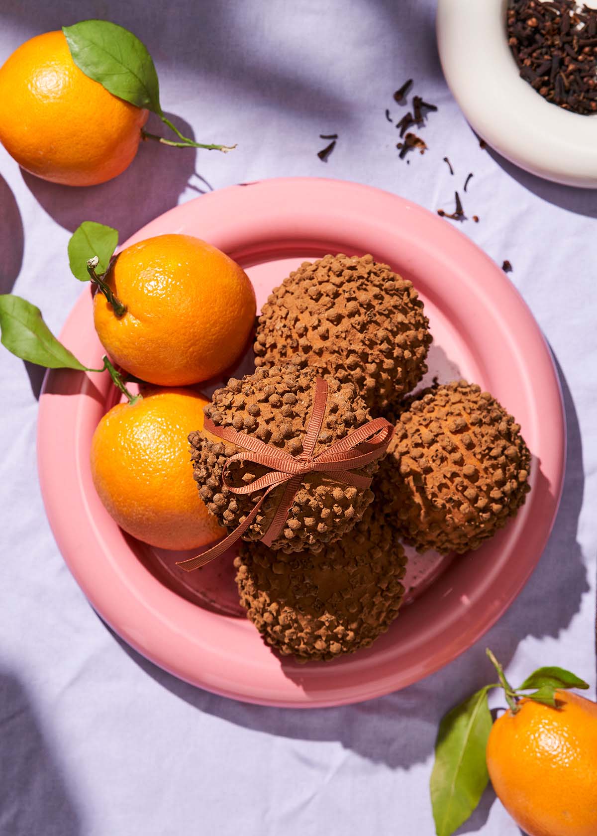 Several orange pomanders on a plate with fresh oranges.