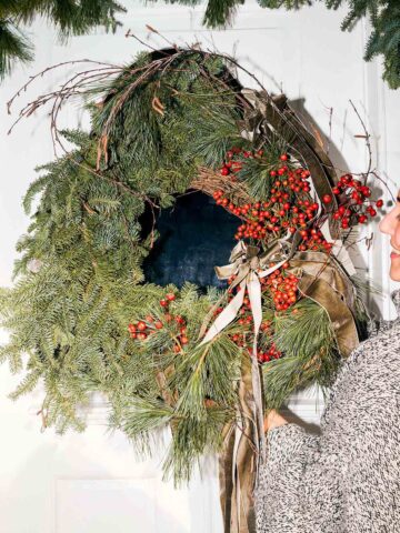 Woman hanging a large evergreen wreath on her door.