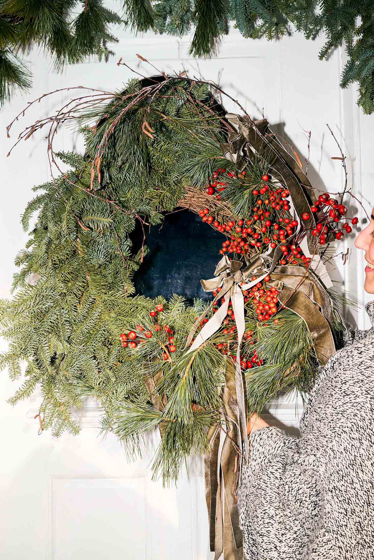 Woman hanging a large evergreen wreath on her door.
